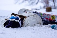 a snowboarder laying in the snow with his head on his back next to another snowboard