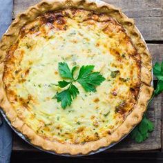 a quiche with cheese and parsley on top sits on a wooden table, ready to be eaten