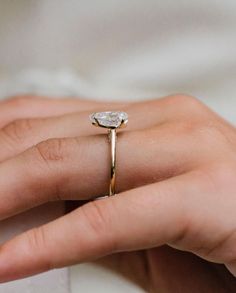 a woman's hand wearing a gold ring with a pear shaped diamond on it