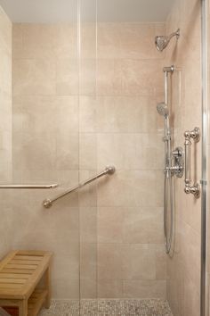 a walk in shower sitting next to a wooden bench on a tiled floor and wall