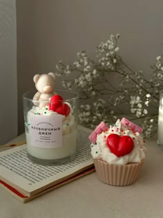 two cupcakes with hearts on them sitting next to a candle and some flowers