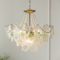 a chandelier with glass beads hanging from it's center point and green plants in the background