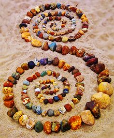 two spirals made out of rocks in the sand with one being surrounded by smaller rocks