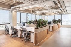 an office with large windows and lots of desks in the center, along with plants