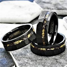 two black rings with gold in them sitting on top of a stone slab next to each other