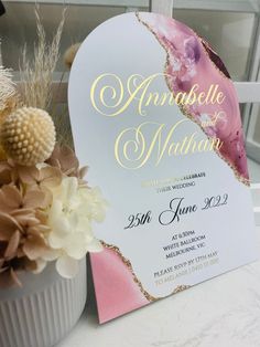 a white and pink heart shaped card with gold foil lettering on it next to flowers