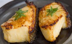 two pieces of cooked fish sitting on top of a black plate next to each other