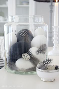 a glass jar filled with black and white eggs on top of a table next to a candle