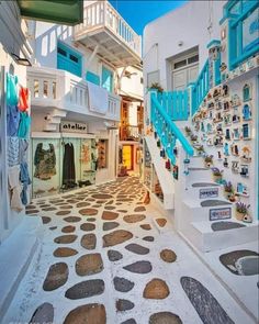 an alley way with blue stairs and white buildings on either side, surrounded by cobblestones