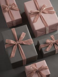 four wrapped gift boxes with pink ribbons and bows on the top, two are grey and one is light pink