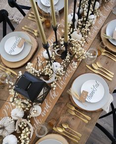 a wooden table topped with white plates and gold place settings next to black candlesticks