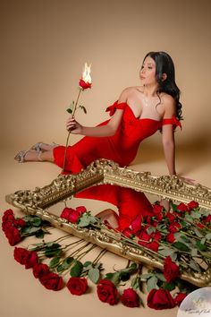 a woman in a red dress is holding a rose and posing for a photo with roses on the floor