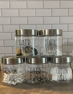 six glass jars with labels on them sitting on a wooden table next to a brick wall