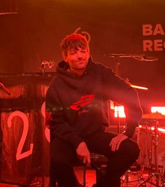 a man sitting on top of a stool in front of a microphone and drum set