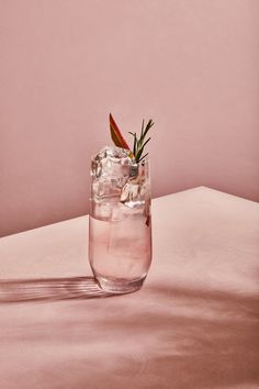 a glass filled with ice and water sitting on top of a white table next to a pink wall