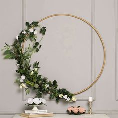 a round gold frame with white flowers and greenery on it next to a table