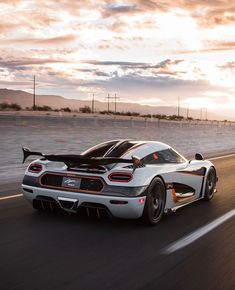 a white and black sports car driving down the road at sunset or sunrise with clouds in the background