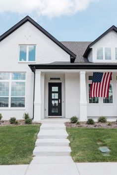 a white house with an american flag hanging on the front door and grass in front