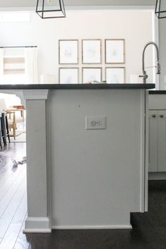 a kitchen island with a black counter top and white cabinets in front of pictures on the wall