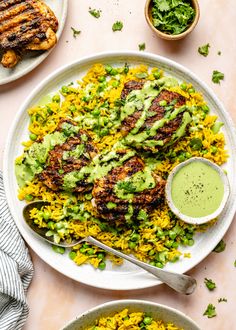 two plates filled with chicken and rice covered in guacamole sauce next to other dishes