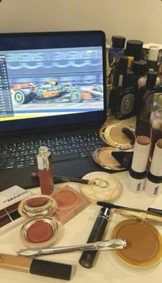 an open laptop computer sitting on top of a white table filled with makeup and cosmetics