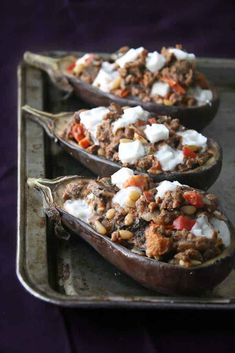 three stuffed eggplant halves on a baking pan with cheese and other toppings