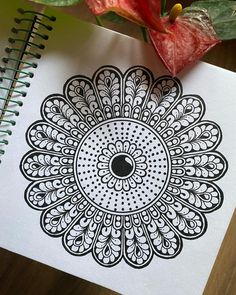 a spiral notebook with an intricate design on it next to a flower potted plant