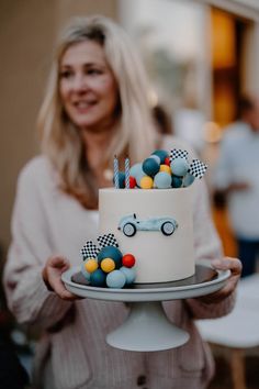 a woman is holding a cake decorated with colorful candies and cars on the top