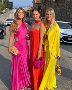 three beautiful women standing next to each other in long dresses and holding purses on the street