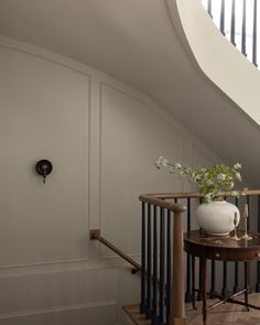 a vase with flowers sitting on top of a wooden table next to a stair case