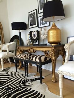 a living room with zebra print rugs and gold accents on the table, along with two white chairs