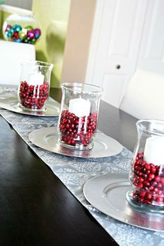 the table is set for christmas with candles and balls in glass vases on it