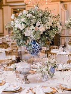 an elegant table setting with white and blue flowers in a vase on the centerpiece