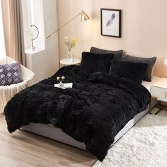 a bed with black comforter and pillows in a room next to a white chair