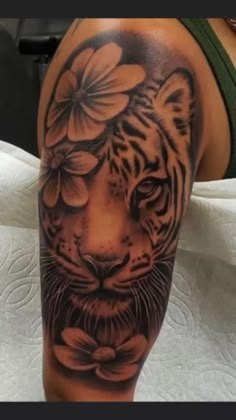 a black and white tiger with flowers on it's head is seen in this tattoo