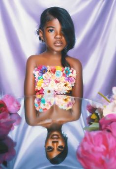 a woman with flowers in her hair is reflected in a glass table surrounded by pink roses