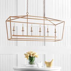 a chandelier hanging over a table with flowers and candles on it in front of a white wall