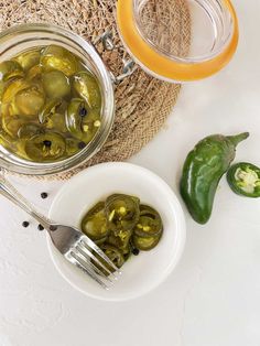 pickles and green peppers sit in bowls next to a glass jar