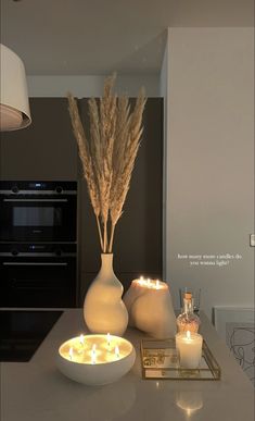 two white vases with lit candles in them on a counter top next to an oven