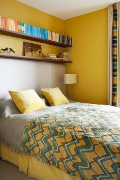 a bed with yellow pillows and blankets in a bedroom next to a book shelf filled with books