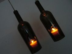 two wine bottles with lights inside them hanging from chains