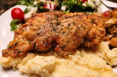 a white plate topped with meat and mashed potatoes next to a green leafy salad