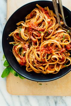 a black bowl filled with pasta and sauce on top of a wooden cutting board next to a knife