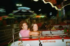 a man and woman are riding on a roller coaster at an amusement park in the night