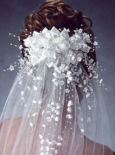 the back of a bride's head with white flowers on it and veil over her shoulder