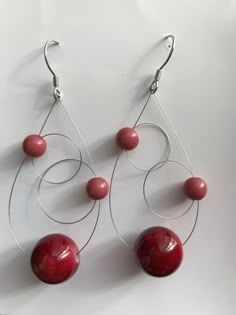 two pairs of red beads hanging from silver hoops on a white surface with metal hooks