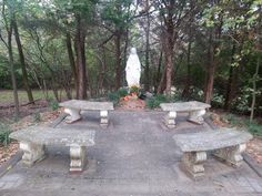 two stone benches sitting on top of a brick walkway in front of trees and a statue