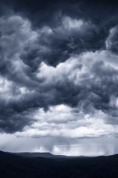 black and white photograph of storm clouds over mountains in the distance, with dark blue sky above