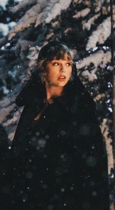 a woman standing in the snow wearing a black coat and looking off into the distance