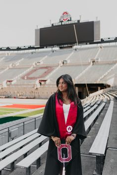 a woman standing in front of a stadium holding a red and black graduation cap, gown, and tassel